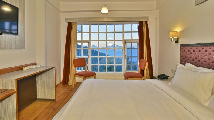 bedroom with large windows, showcasing natural light through open curtains at DLS Hillcrest Resort, Shimla